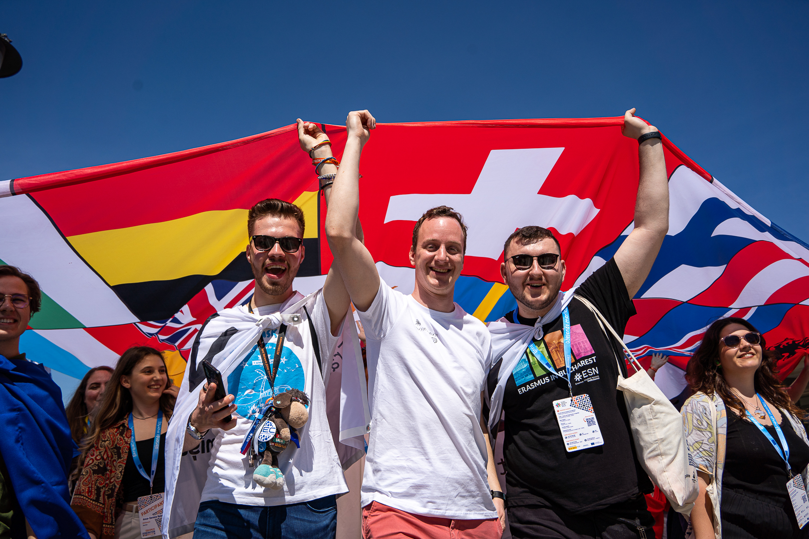 A group of young people holding a big flag made of many other country flags.