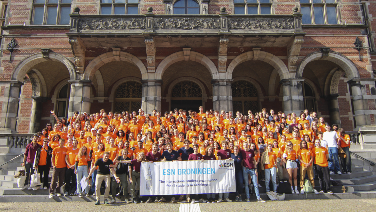 A big group of people in orange shirts posing for a picture and holding a flag of ESN Groningen.