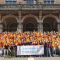 A big group of people in orange shirts posing for a picture and holding a flag of ESN Groningen.