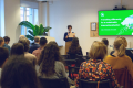 A photo of a person speaking in front of an audience.