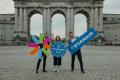 Three people, standing in front of a large stone arch monument, each holding oversized colourful props: the Erasmus Student Network logo, a circular Ryanair–ESN logo, and a rectangular Ryanair sign.