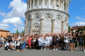 A big group of people posing for a photo in front of the Leaning Tower of Pisa.